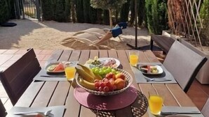 Un área de comedor al aire libre con mesas y sillas de madera, un frutero y platos con comida y bebidas.