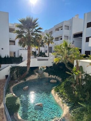 Un patio con una piscina cristalina, rodeado de edificios blancos y palmeras.