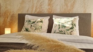 Una cama con cabecera texturizada, dos almohadas con estampado de hojas tropicales y decoración con plumas de plumas.