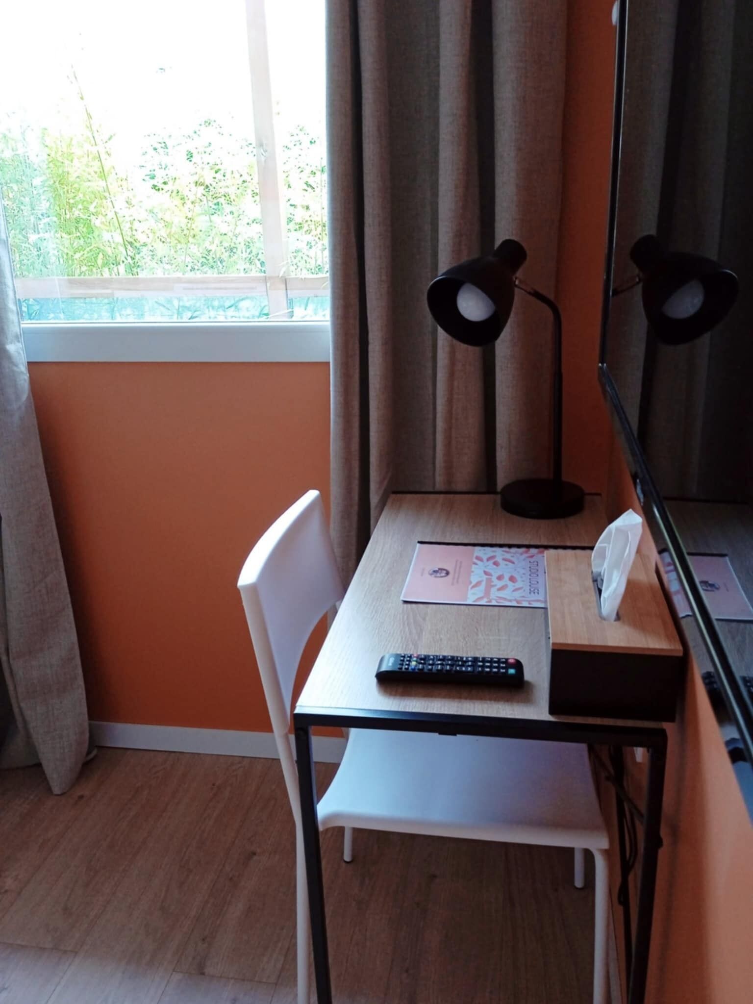 Een kamer met een houten tafel, een witte stoel, een afstandsbediening, een zakdoekendoos en een spiegel.