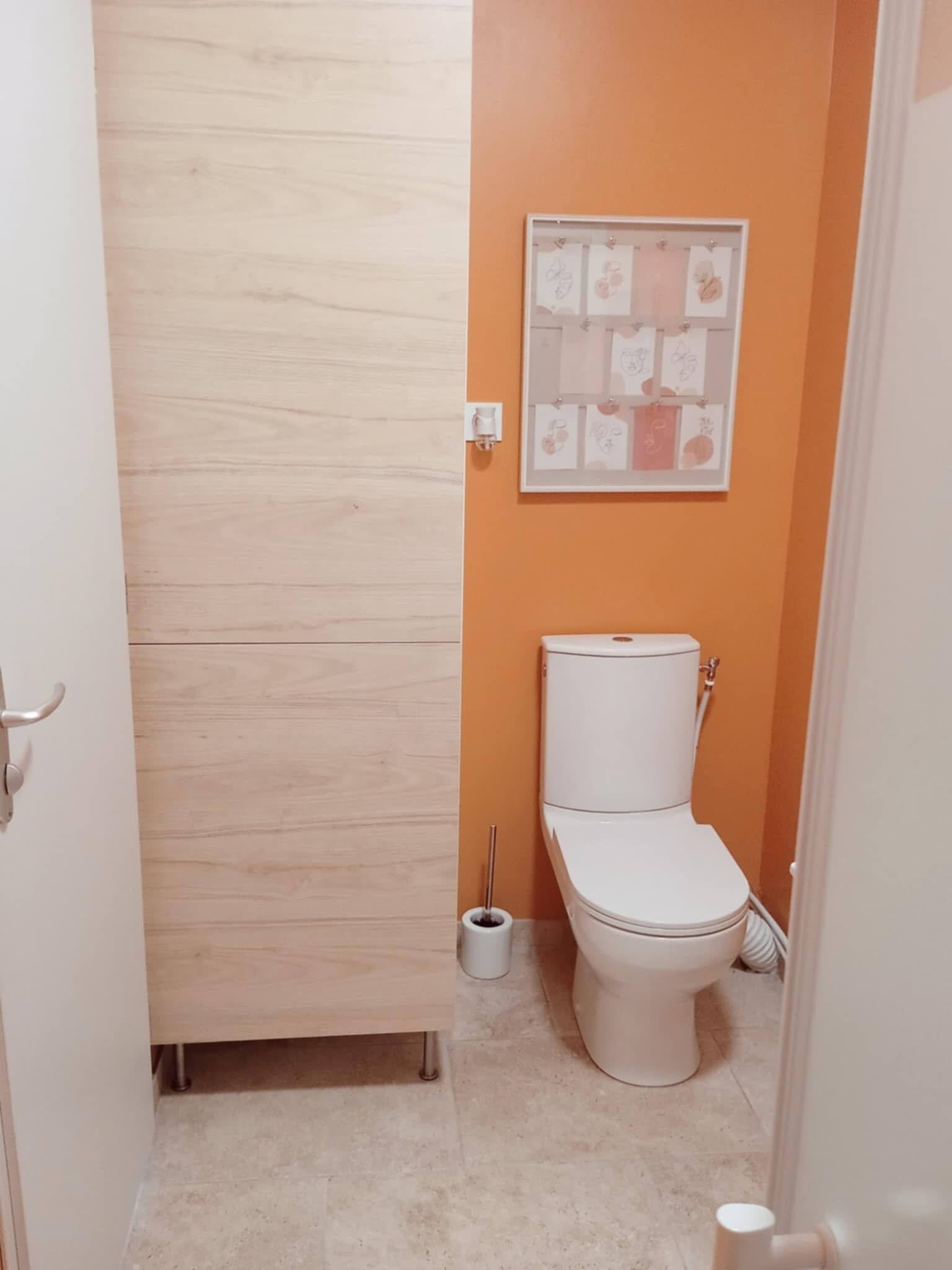 Ein kleines Badezimmer mit Toilette, einem Toilettenpapierhalter an der Wand und einer Holztür.