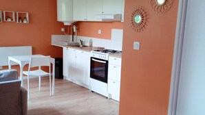 A modern kitchen with white cabinets, a stove, and a dining area with a table and chairs. - Studio L'with terrace (Oyonnax)