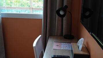 A small room with a single table, a chair, a desk lamp, a remote control, and a television.