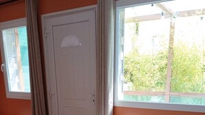 A room with a grey sofa, a white door, and a window with a view of greenery. - Studio L'with terrace (Oyonnax)