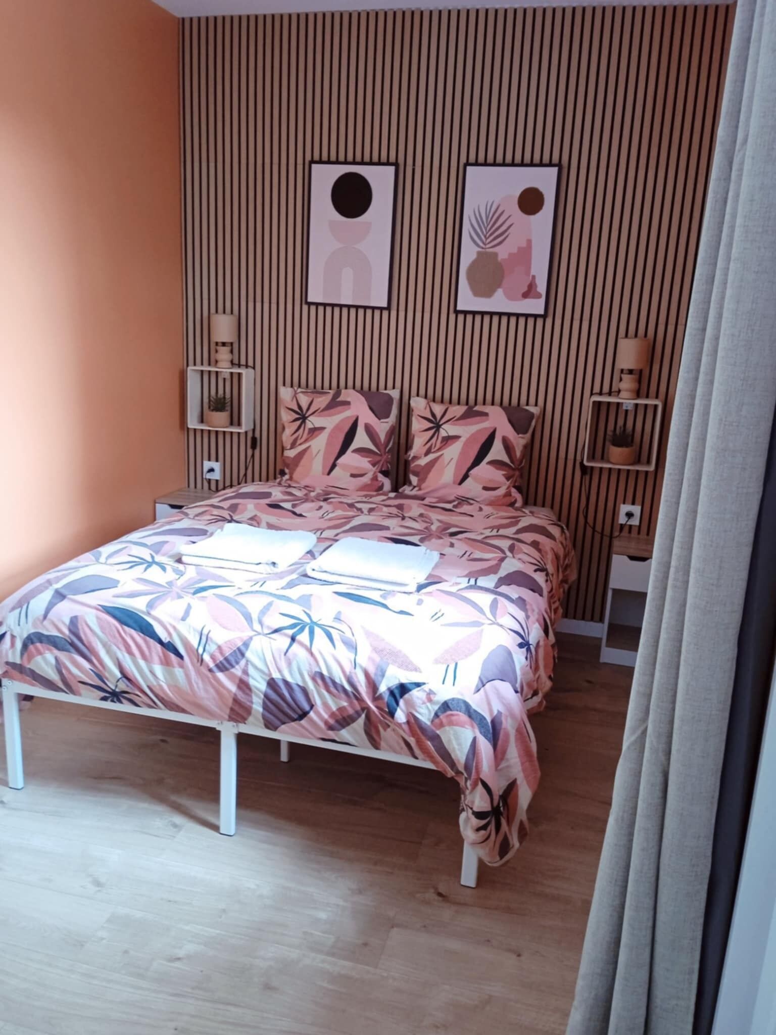 Un dormitorio con una cama, un revestimiento de madera en la pared y dos estantes fijos a la pared con lámparas.