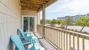 Un balcon abrité avec des balustrades en bois, une porte-fenêtre coulissante et des fauteuils Adirondack bleus.