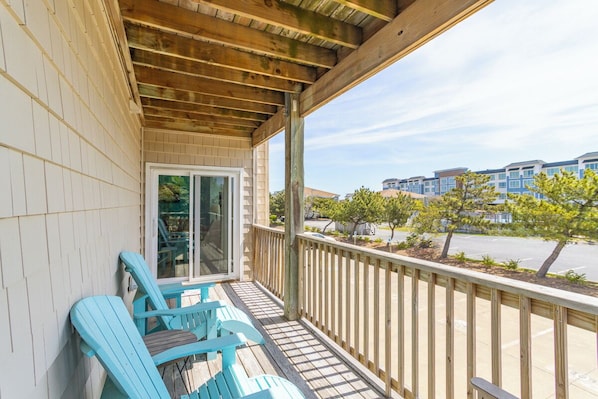 A covered balcony with wooden railings, a sliding glass door, and blue Adirondack chairs. - Pet-friendly, centrally-located oceanside condo w/ community pool! (Kill Devil Hills)