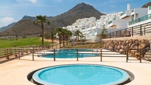 A pool area with two circular pools, surrounded by a low stone wall and palm trees, with a mountain in the background. - Casa Sierra Golf - Two Bedroom Apartment, Sleeps 4 (Pulpí)