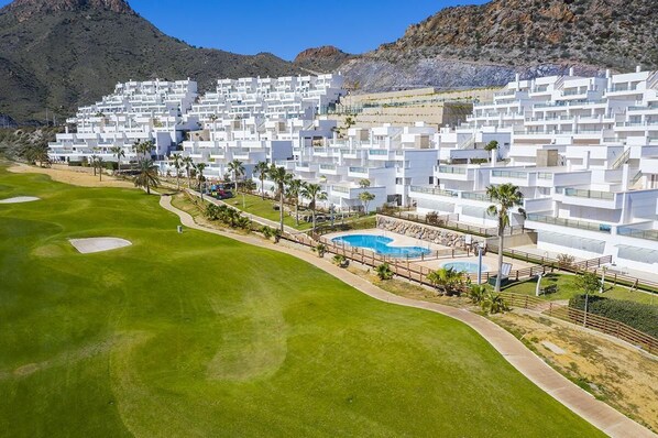 A modern resort with white buildings, a swimming pool, and a golf course.