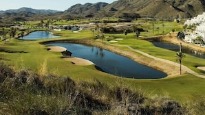 Ein Golfplatz mit mehreren Teichen, einem Clubhaus und einer Bergkulisse im Hintergrund.