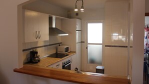 Una cocina con encimeras de madera, microondas, estufa y alacenas. Hay una ventana con vidrio esmerilado y una puerta que da a otra habitación.