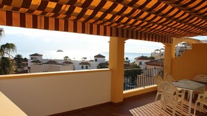 Un espacio al aire libre techado con una mesa y sillas, con vistas a una ciudad costera con edificios y palmeras.