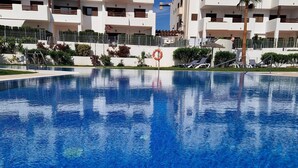 A swimming pool with clear blue water, surrounded by a tiled deck and a white building with balconies in the background. - Casa Roberto - Two Bedroom Apartment, Sleeps 4 (Pulpí)