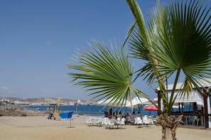 Een restaurant aan het strand met terras, palmbomen en uitzicht op zee.