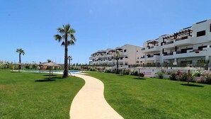 A pathway leading to a modern building with multiple balconies and a pool area with palm trees. - Casa Roberto - Two Bedroom Apartment, Sleeps 4 (Pulpí)