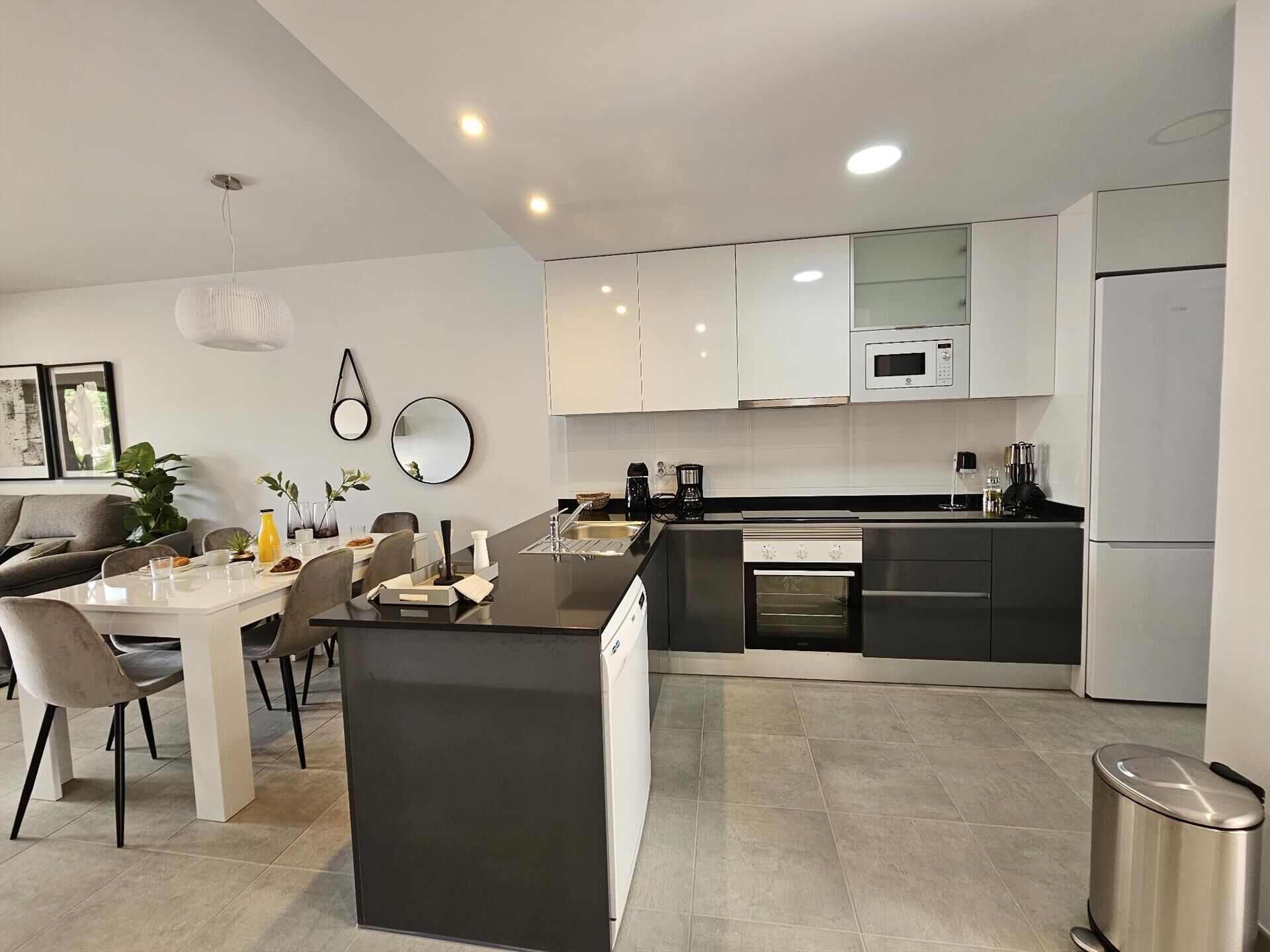 A modern kitchen with white cabinets, a central island, and a dining area with a table and chairs.