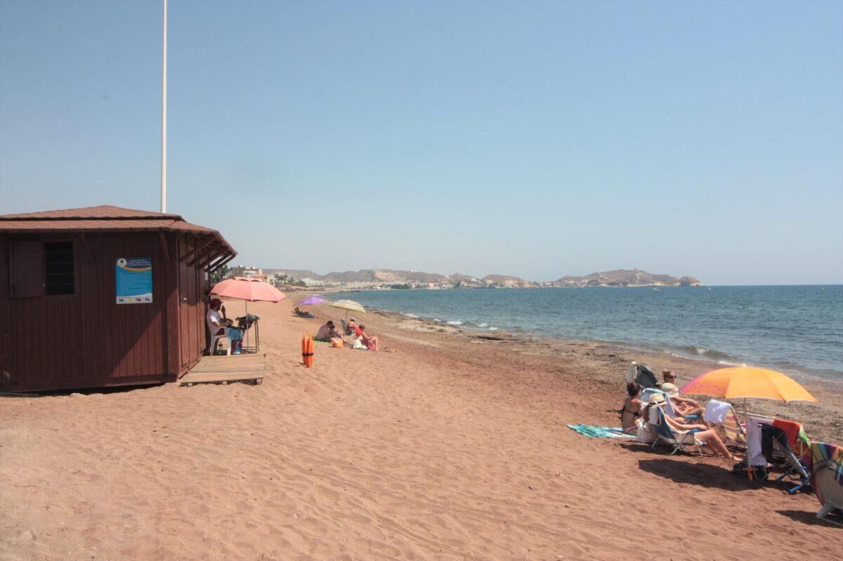 A beach with a wooden building, beach chairs, and umbrellas.