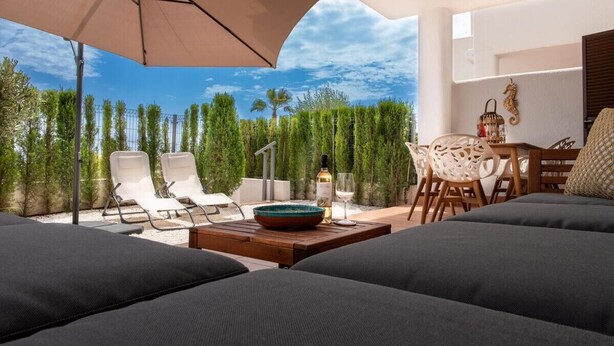 Un espace extérieur moderne, aménagé avec un grand parasol, des fauteuils confortables et une table à manger avec des chaises.