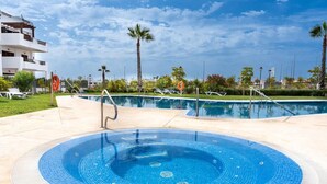 Une piscine avec un jacuzzi, entourée de chaises longues et de palmiers.