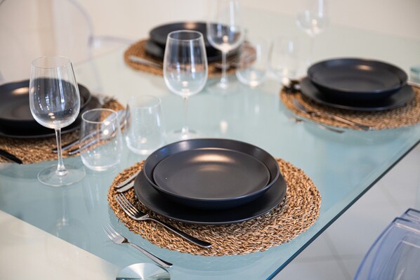 A table set with black plates, clear glasses, and silverware on a glass table with woven placemats.