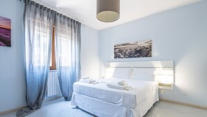 A bedroom with a bed, curtains, a headboard, a wall-mounted light, and a window. - Holiday Home 'P012' with Balcony, Wi-Fi and Air Conditioning (Cagliari)
