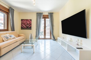A living room with a sofa, a glass coffee table, a TV on the wall, and a balcony door. - Holiday Home 'P012' with Balcony, Wi-Fi and Air Conditioning (Cagliari)
