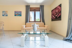 Un soggiorno con un divano, un tavolino in vetro, un quadro di una rosa e una finestra con tende.
