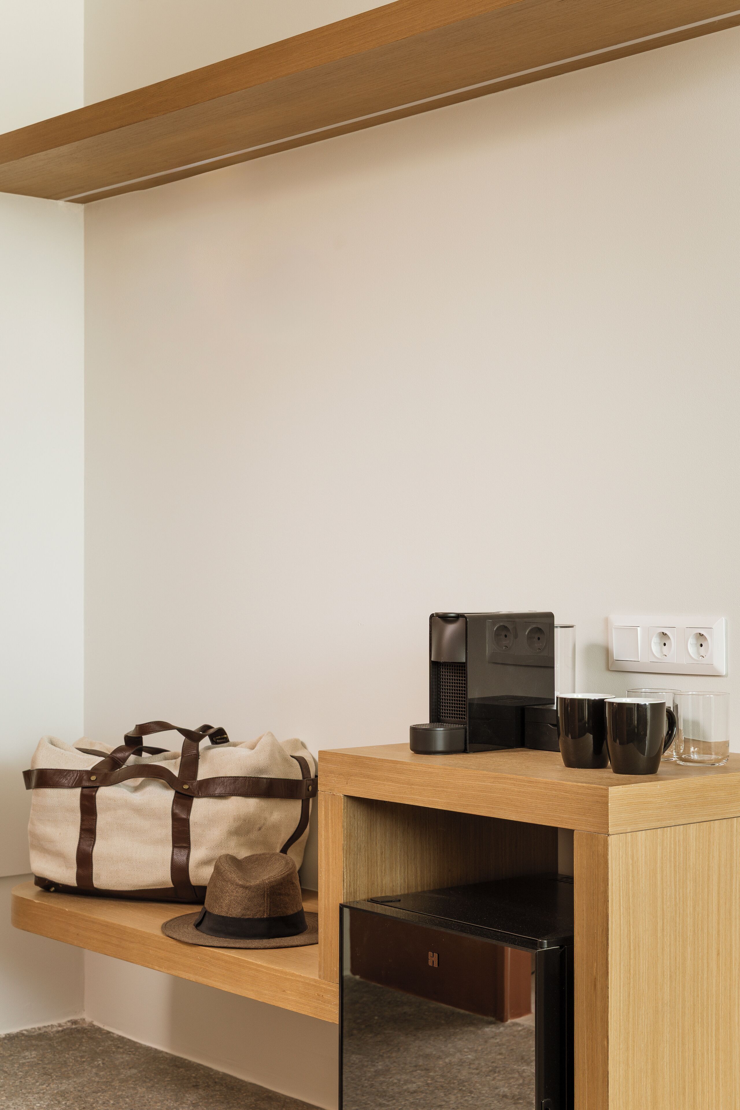 A wooden desk with a coffee maker, a bag, and a hat.