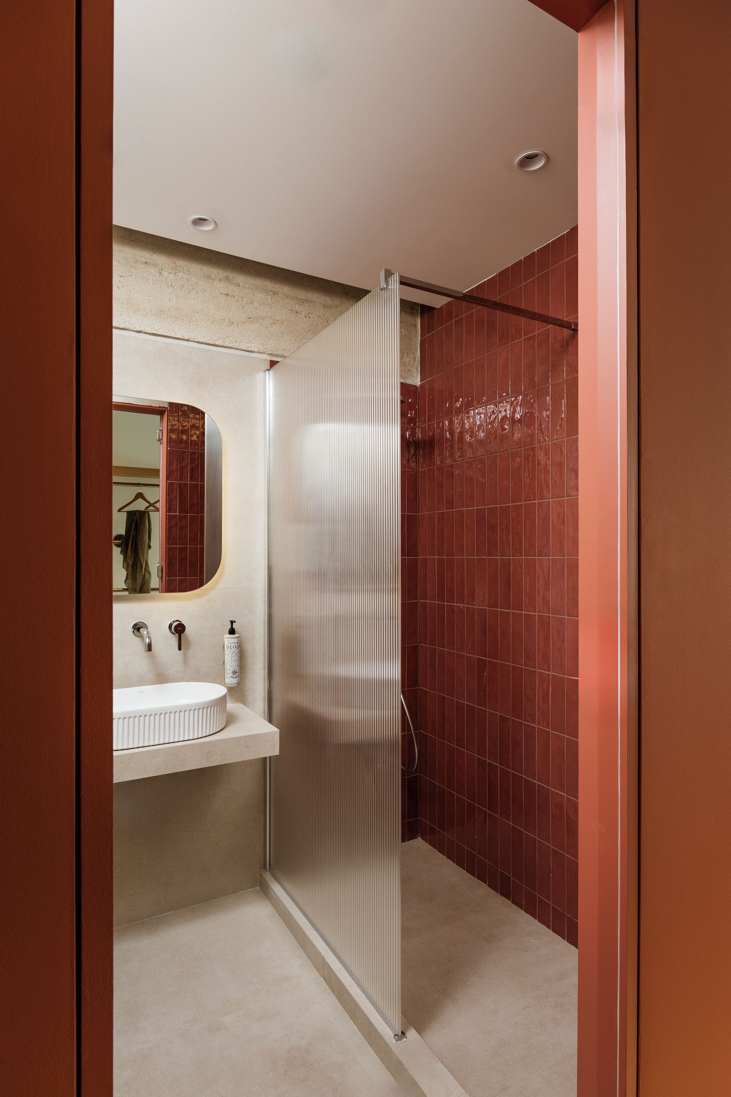 Een badkamer met een wit wastafel, een spiegel, een douchecabine en rode betegelde wanden.