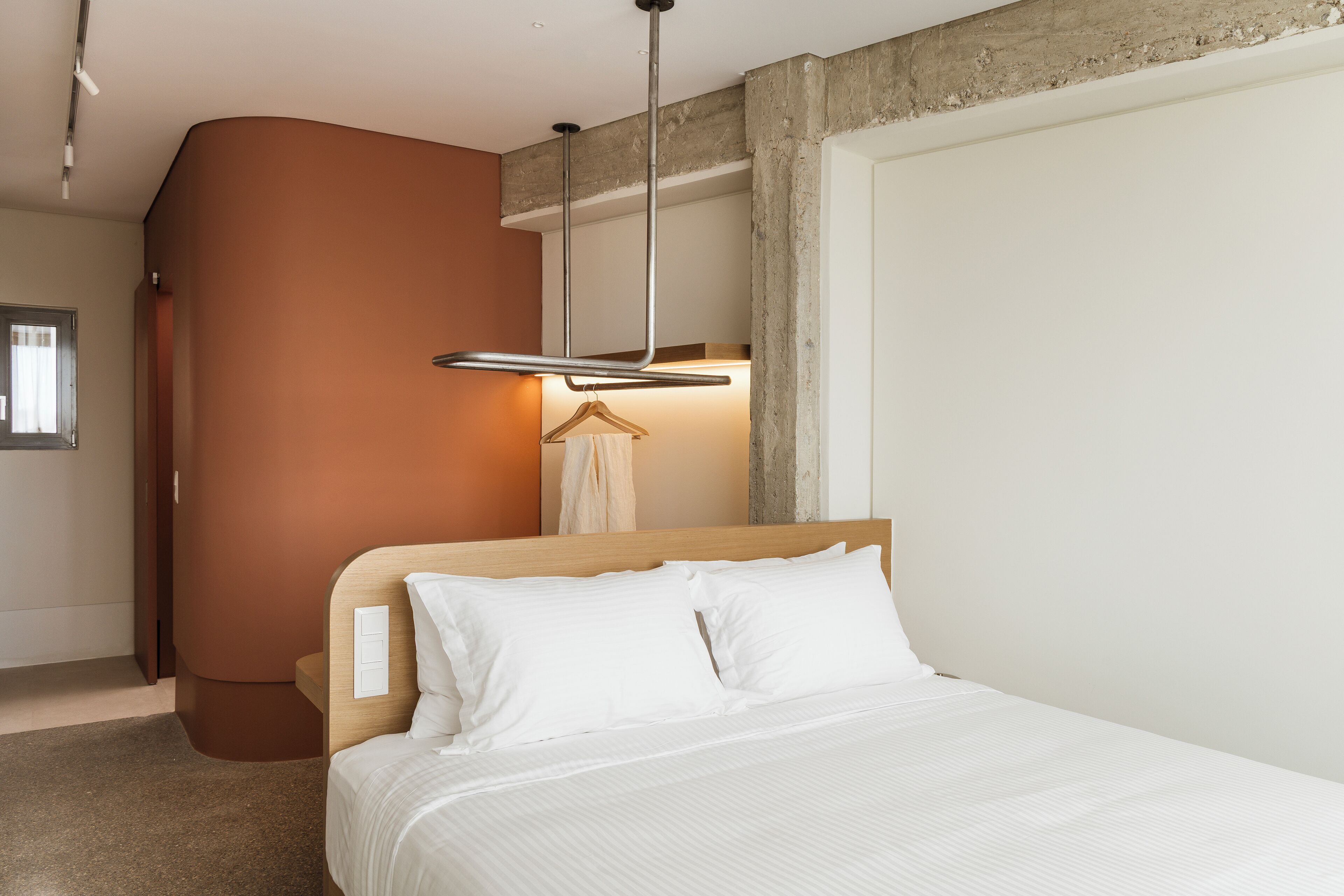Un dormitorio con cama, cabecera de madera, lámpara colgante y toallero de pared.