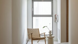 Ein moderner, minimalistischer Raum mit einer gebogenen Sitzbank, einem Holzstuhl und einem kleinen Tisch mit Pflanze.
