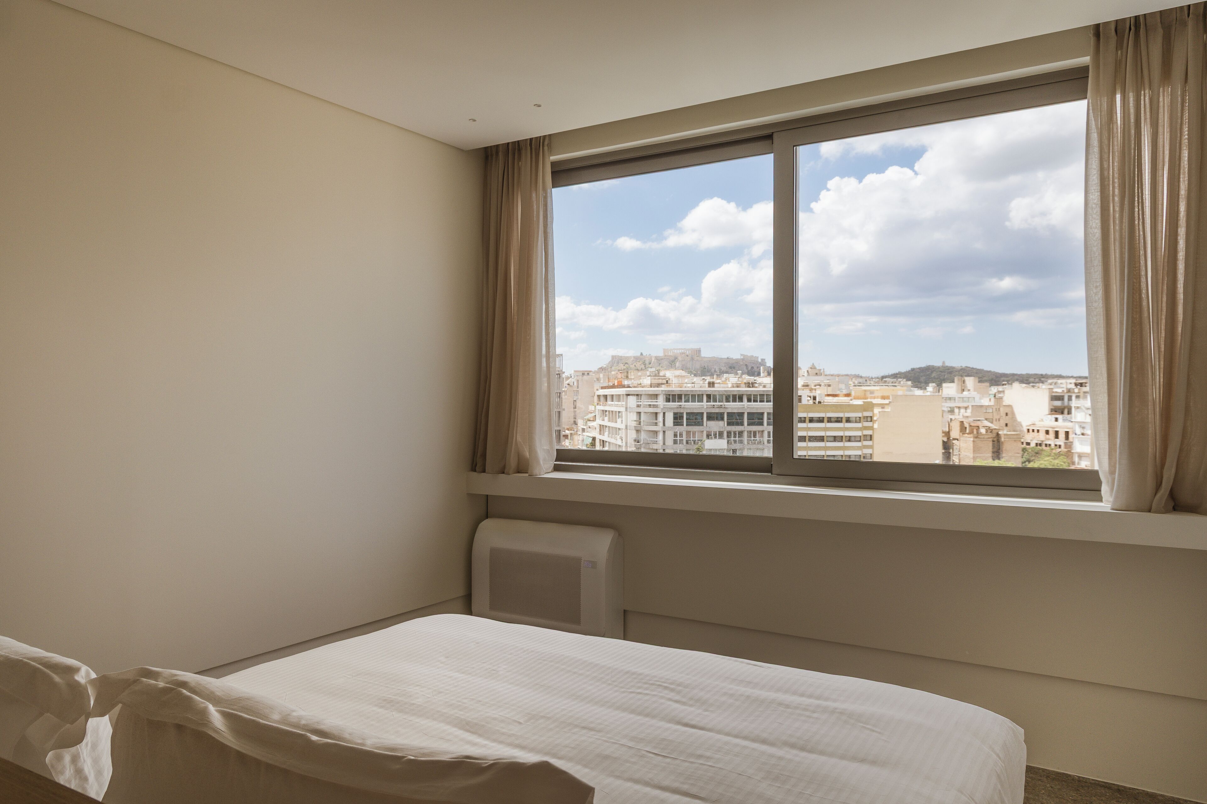 A hotel room with a bed, a window with curtains, and a view of a cityscape.