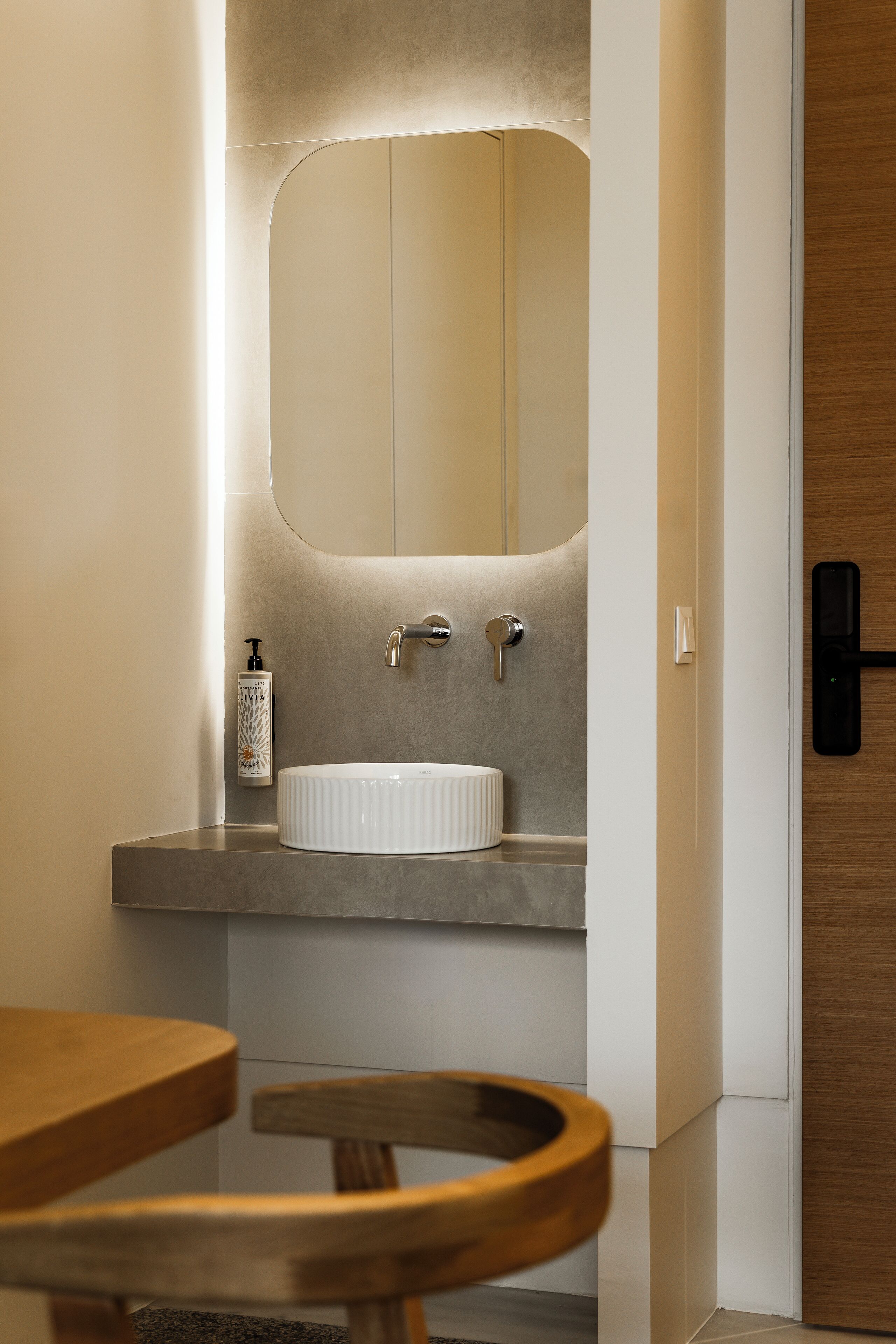 Un baño moderno con un lavabo blanco, un espejo grande y una puerta de madera.