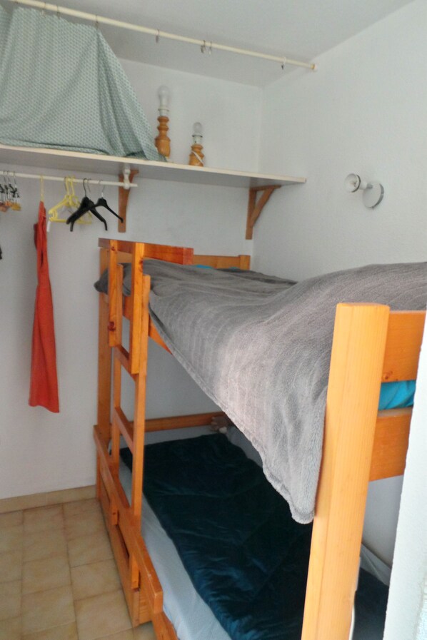A bunk bed with a grey mattress, wooden frame, and a blue blanket at the bottom.