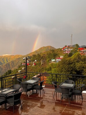 A terrace with outdoor seating, overlooking a hillside with buildings and a mountain. - The Grand Resort (Dhanaulti)