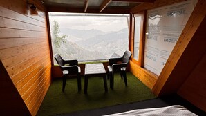A room with a bed, a small table, two chairs, and a view of mountains through a window. - The Grand Resort (Dhanaulti)