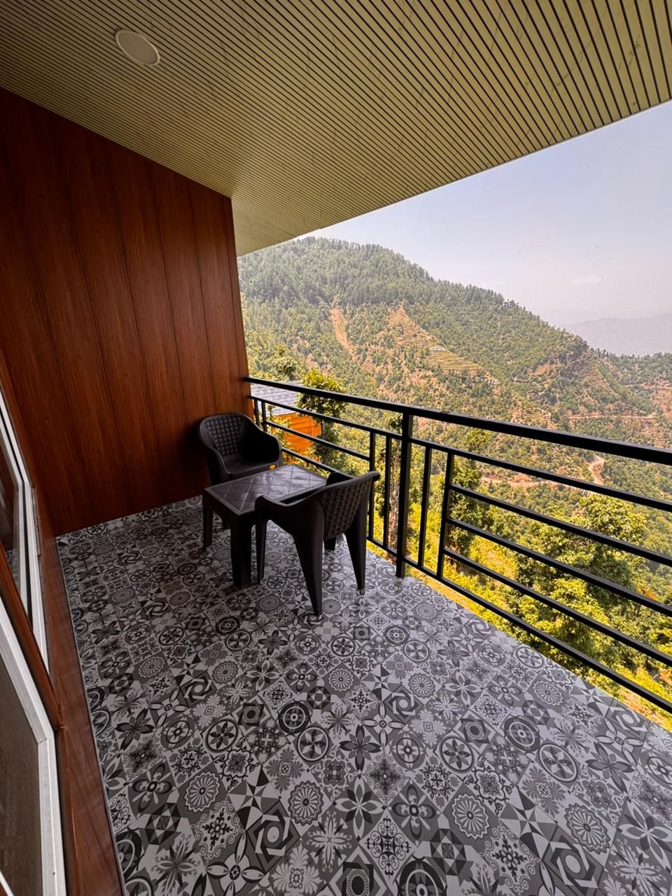 Un balcón con suelo estampado, una mesa y dos sillas. El balcón ofrece vistas a un paisaje montañoso.