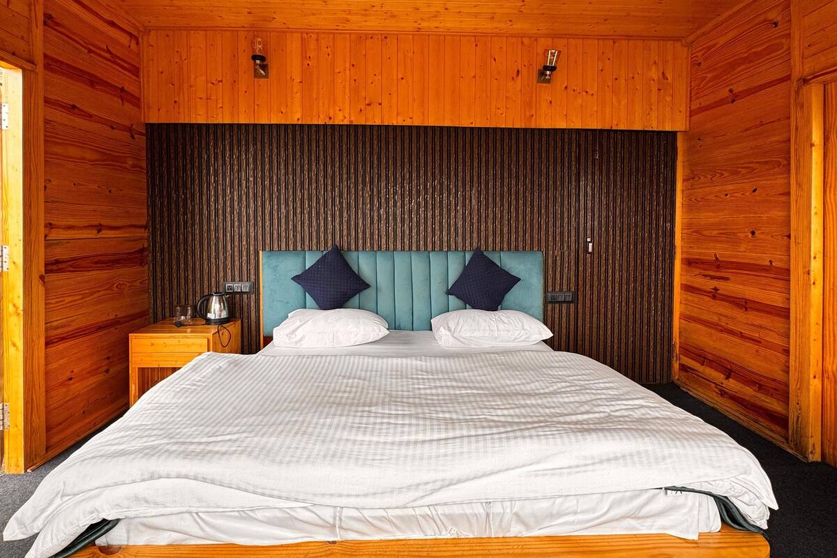 Ein Schlafzimmer einer Holzhütte mit einem Bett, zwei Kissen, einem Nachttisch und einer Wandleuchte.