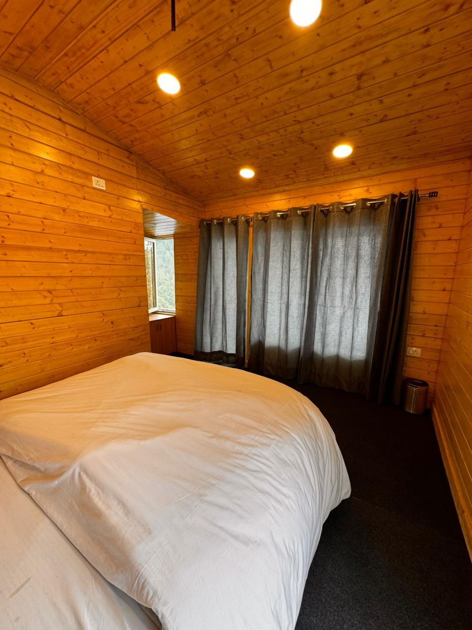 Una habitación de cabaña de madera con una cama grande, paredes de madera y una ventana con cortinas.