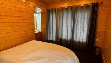 Una habitación de cabaña de madera con una cama grande, paredes de madera y una ventana con cortinas.