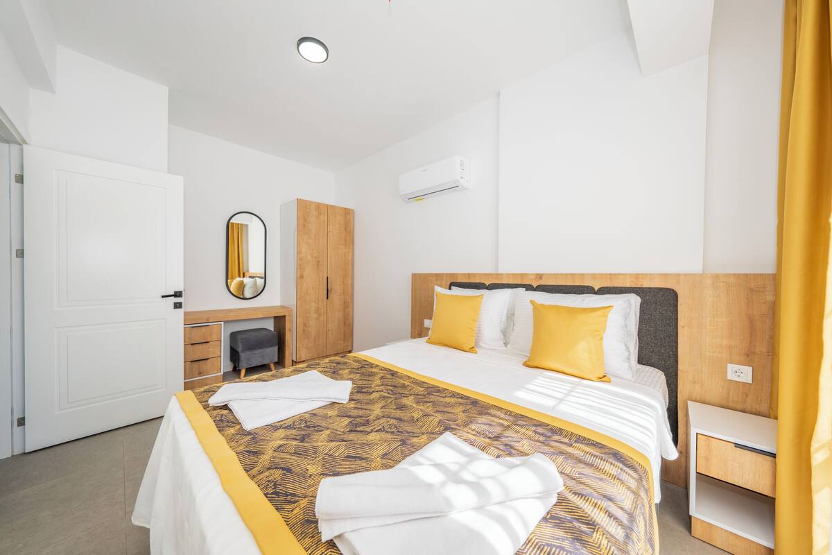 A hotel room with a large bed, a wooden wardrobe, a mirror, and a bedside table.