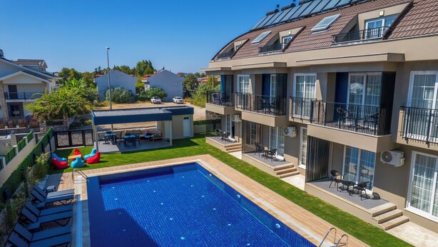 A residential building with a swimming pool, outdoor seating, and multiple balconies. - Dede Suites Fethiye (Fethiye)