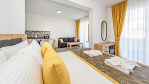 A modern hotel room with a large bed, a small desk, a sofa, and a kitchenette in the background. - Dede Suites Fethiye (Fethiye)