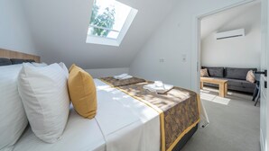 A bedroom with a skylight, a bed with white and yellow pillows, a sofa, and an air conditioning unit. - Dede Suites Fethiye (Fethiye)