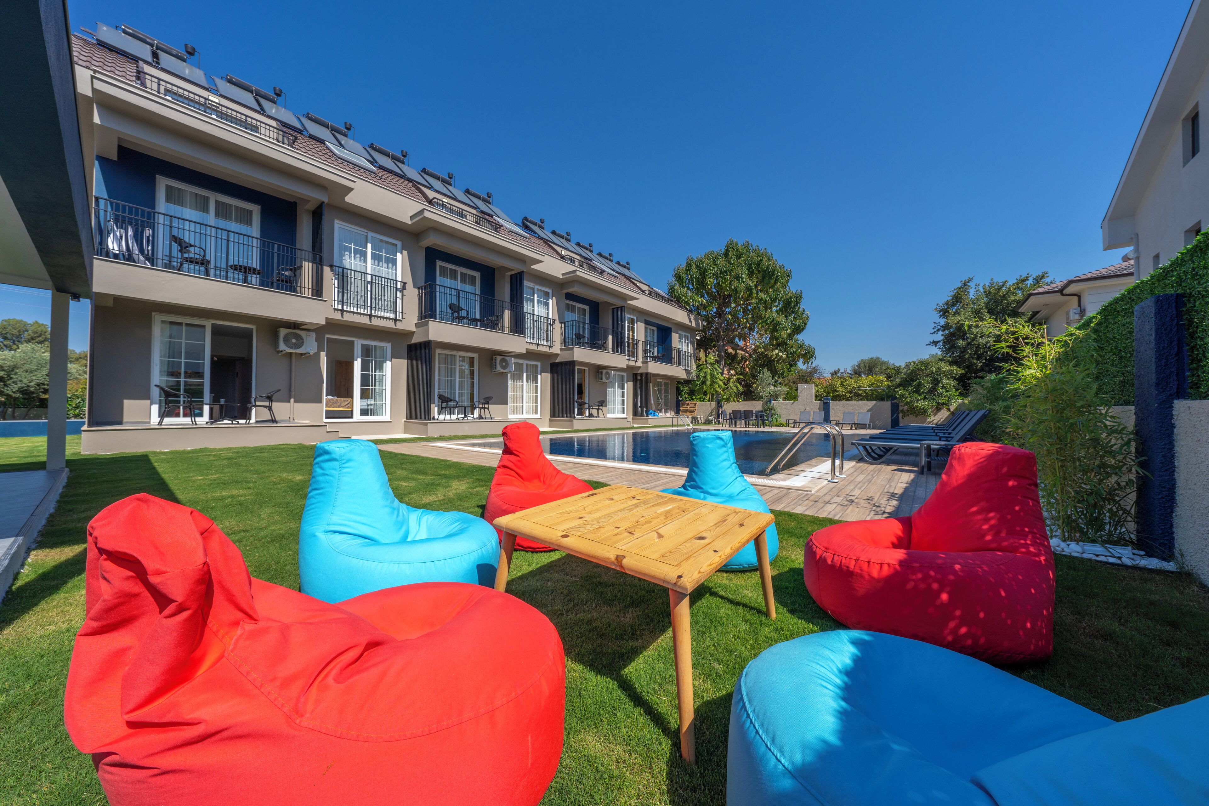 A modern apartment complex with a swimming pool, outdoor seating area with colorful bean bags, and a well-maintained lawn.