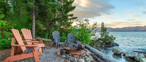 Eine Sitzgelegenheit am Seeufer mit Adirondack-Stühlen und einem Feuerkorb.