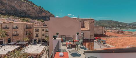 Una terraza en la azotea con mobiliario exterior, vistas del pueblo y un acantilado al fondo.