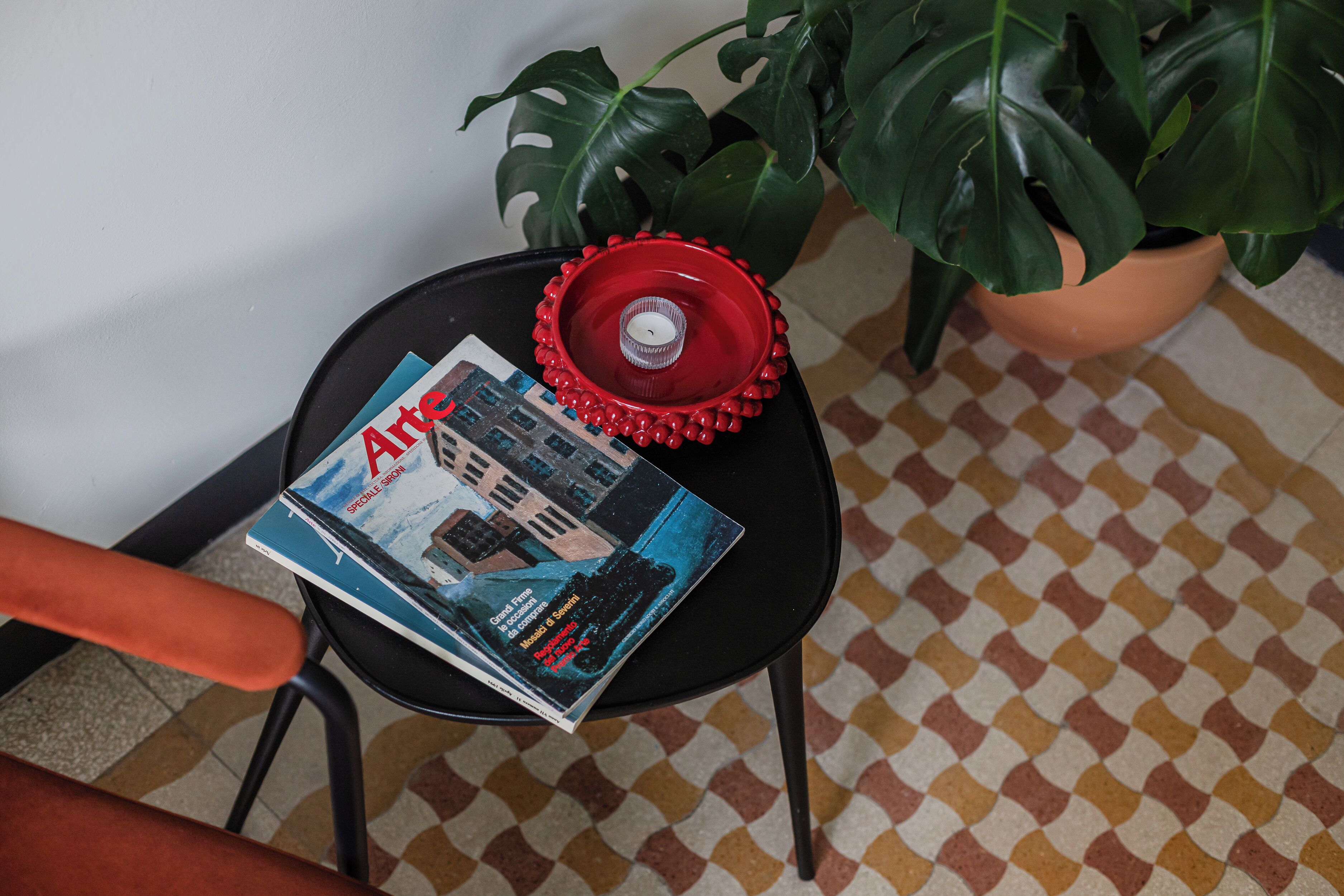 A magazine on a black table with a red decorative item and a potted plant beside it.