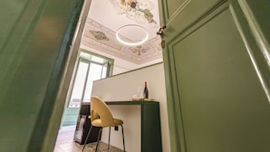 A room with a green door, a chandelier, a chair, and a table with a bottle and glasses. - Palazzo Villelmi (Cefalù)