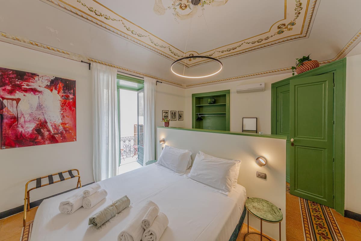Habitación de hotel con una cama grande, un armario verde, un taburete pequeño y un cuadro en la pared.